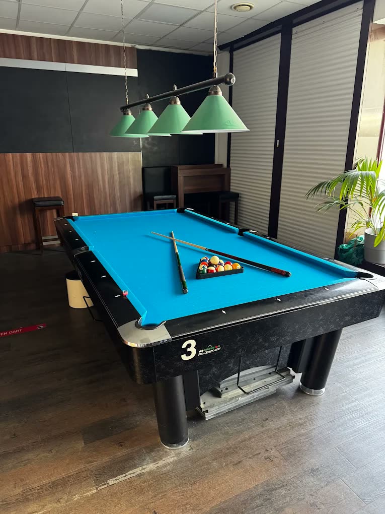 Pool-стол с синей тканью рядом со стеной и подвесными лампами в Billard O.